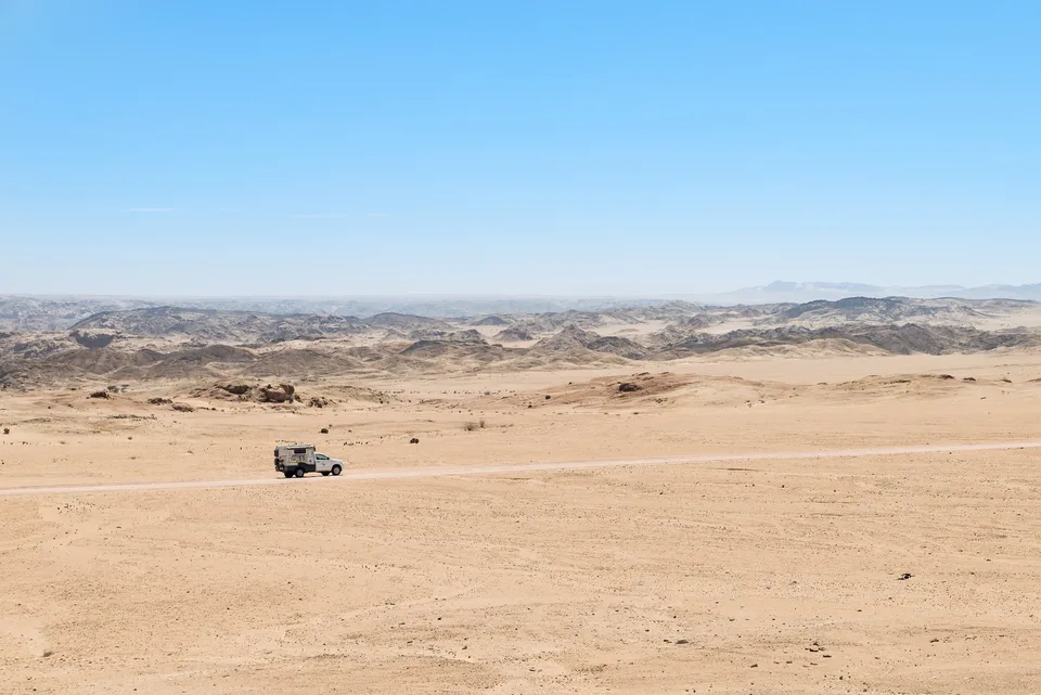 Kleiner Camper in einer weiten hellen Wüstenlandschaft.