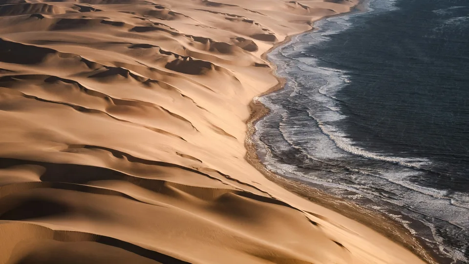 Sanddünen treffen unmittelbar auf die dunkle Brandung des Ozeans.